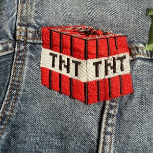 May include: A red and black embroidered patch of a Minecraft TNT block with the text "TNT" on the front.