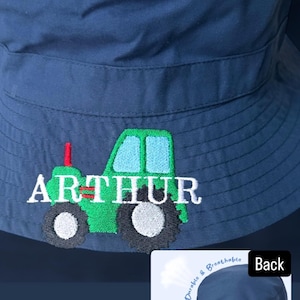May include: A blue bucket hat with an embroidered green tractor and the name "ARTHUR". The hat has an adjustable buckle and is made of 100% polyester.