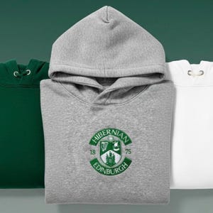May include: Three hooded sweatshirts in green, gray, and white. The gray sweatshirt features a green and white embroidered emblem with the text "HIBERNIAN EDINBURGH 1875". Each sweatshirt has a drawstring hood.