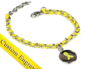 May include: A yellow ribbon charm bracelet with a silver chain and a yellow ribbon charm. The charm has a yellow ribbon on a silver background. The bracelet is on a white background.