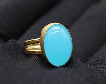 May include: A gold ring featuring a large, oval, turquoise-coloured stone. The ring has a double band design and a smooth, polished finish. The stone is set in a gold bezel.