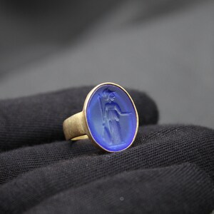 May include: A gold ring with a blue oval cameo featuring a carved image of a woman.