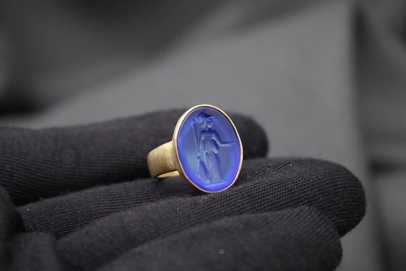 May include: A gold ring with a blue oval cameo featuring a carved image of a woman.