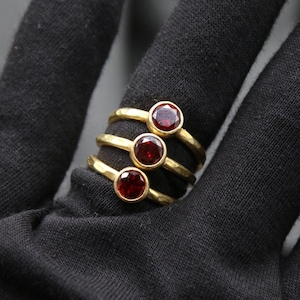 May include: Three gold rings with red gemstones. The rings are stacked on top of each other.