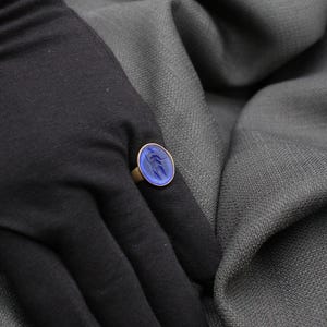 May include: A gold ring with a blue oval-shaped stone set in the center. The stone has a swirling pattern.