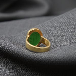 May include: A gold ring with a green oval gemstone. The ring is on a gray fabric background.