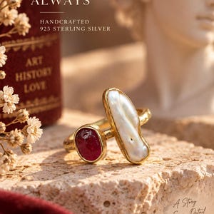 May include: A gold-toned ring featuring a long, irregular white pearl and a small, oval-shaped deep red gemstone. The band has a textured, hammered finish. The ring is displayed with text that reads UNIQUE BEAUTY ALWAYS, HANDCRAFTED 925 STERLING SILVER, and A Story in Every Detail.