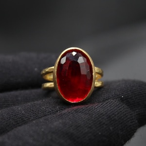 May include: A gold ring with a large, oval-shaped, red gemstone.