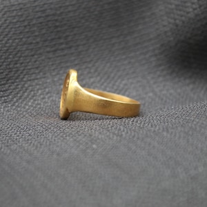 May include: A gold signet ring with a smooth, oval-shaped top. The ring is shown from the side, with the band facing the viewer.