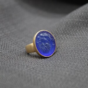 May include: A gold ring with a blue oval-shaped stone. The stone has a carved design.