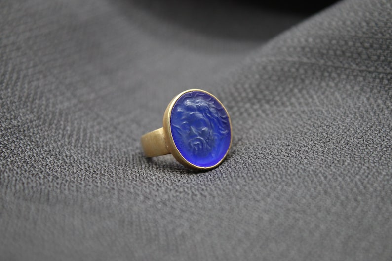 May include: A gold ring with a blue oval-shaped stone. The stone has a carved design.