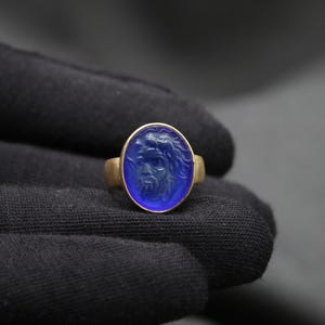 May include: A gold ring with a blue oval-shaped stone featuring a carved face.