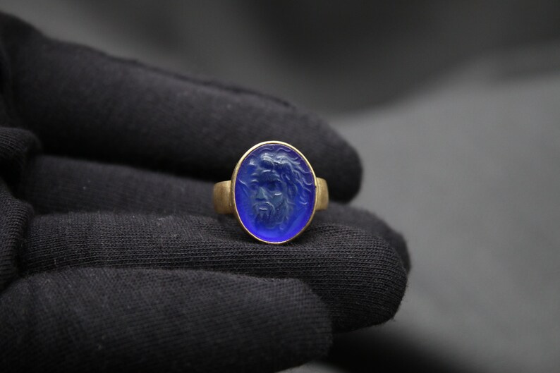 May include: A gold ring with a blue oval-shaped stone featuring a carved face.