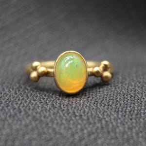 May include: A gold ring with an oval-shaped green opal gemstone. The ring has three small gold balls on each side of the stone.