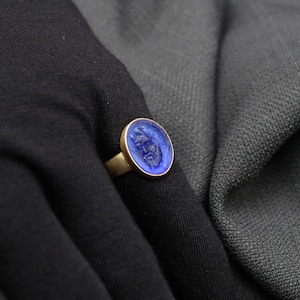 May include: A gold ring with a blue glass cameo featuring a carved face.
