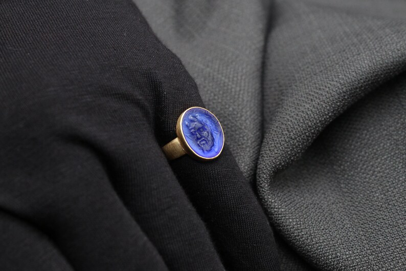 May include: A gold ring with a blue glass cameo featuring a carved face.