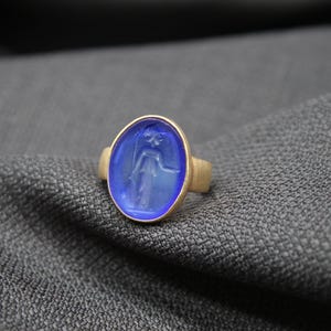 May include: A gold ring with a blue oval-shaped gemstone featuring a carved design of a person.