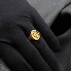 May include: A gold ring with a detailed design of two figures holding hands. The ring is worn on a person's finger.