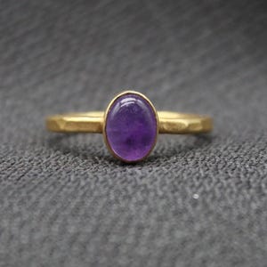 May include: A gold ring with a purple oval amethyst gemstone.