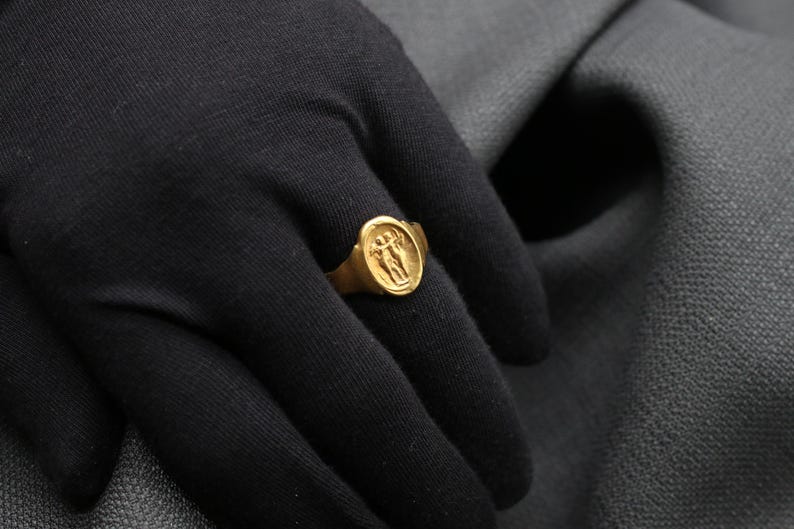 May include: A gold ring with a raised design of two figures holding hands. The ring is worn on a person's finger.
