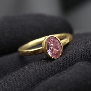 May include: A gold ring with a hammered texture and a pink oval gemstone.
