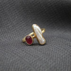Puede incluir: Anillo de oro con una perla blanca y una piedra roja.