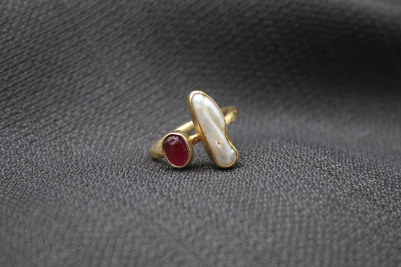 Puede incluir: Anillo de oro con una perla blanca y una piedra roja.