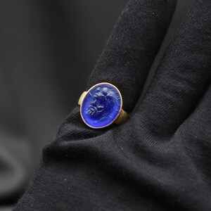 May include: A gold ring with a blue glass cameo featuring a carved design. The cameo is oval shaped and set in a gold bezel.