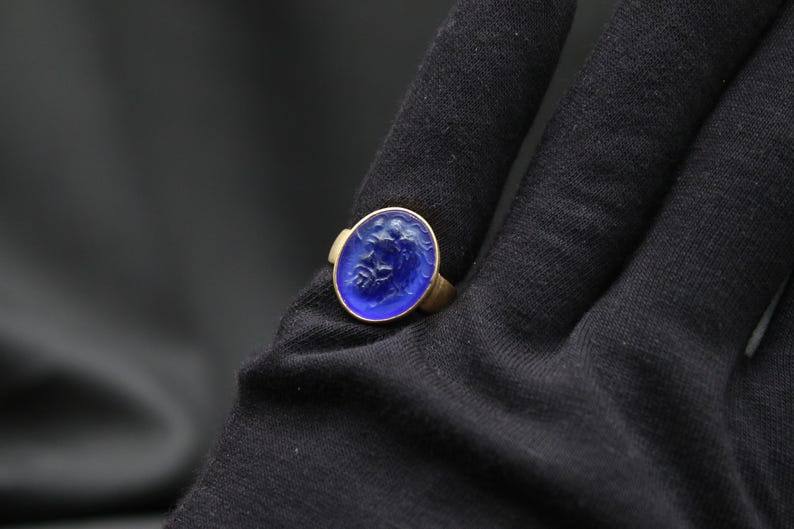 May include: A gold ring with a blue glass cameo featuring a carved design. The cameo is oval shaped and set in a gold bezel.