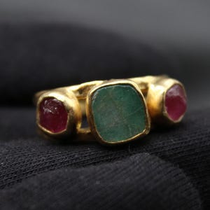 Peut inclure: Une bague en or sertie de trois pierres précieuses. La pierre centrale est une grande émeraude verte. Les deux pierres plus petites de chaque côté sont des rubis rouges.