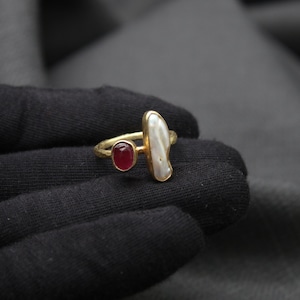 Puede incluir: Anillo de oro con una perla blanca y una piedra roja.