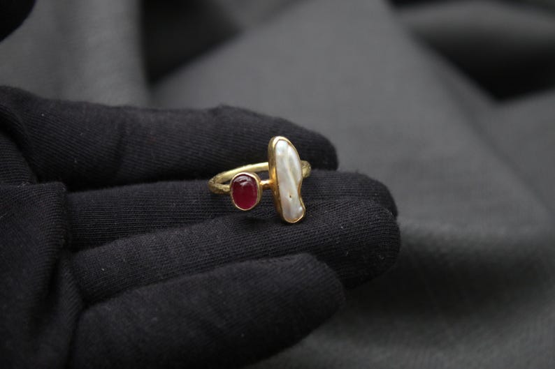Puede incluir: Anillo de oro con una perla blanca y una piedra roja.
