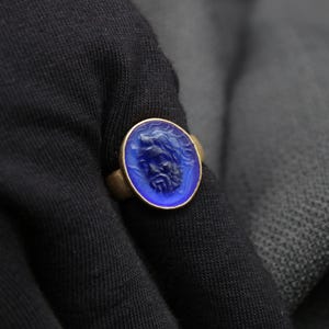 May include: A gold ring with a blue glass cameo featuring a carved face.