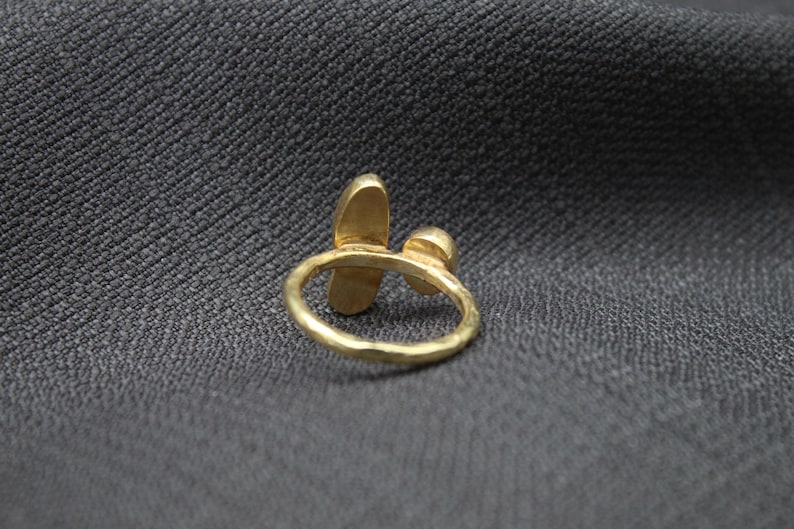 Puede incluir: Un anillo de oro con dos piedras en forma de l&aacute;grima. El anillo est&aacute; hecho de metal martillado y tiene un dise&ntilde;o simple y elegante.