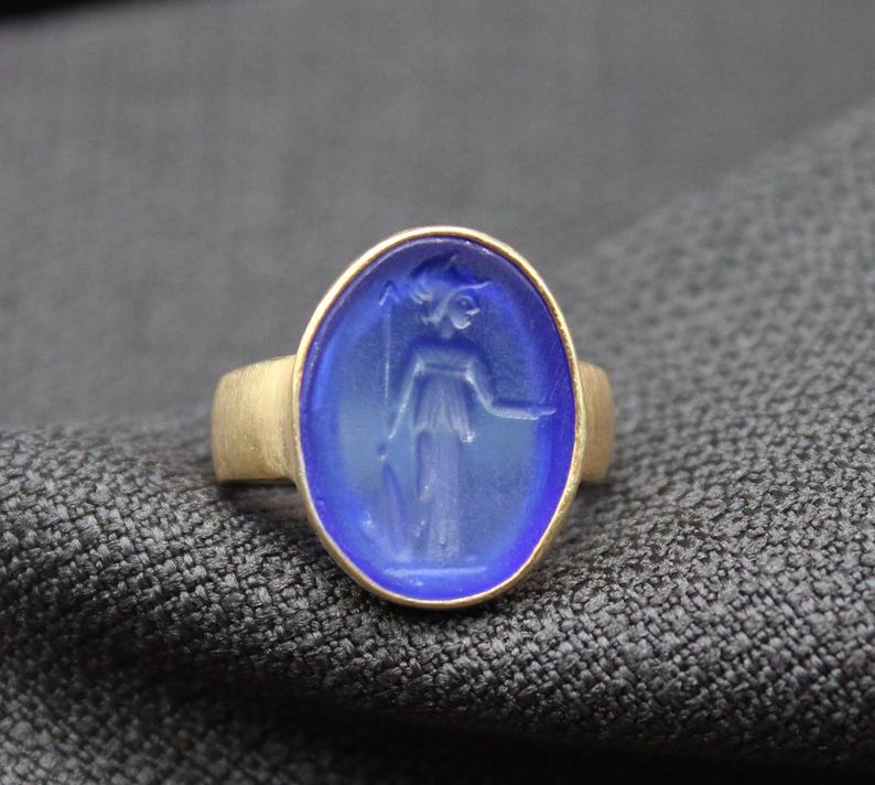 May include: A gold ring with a blue oval cameo featuring a carved image of a woman in a flowing robe.