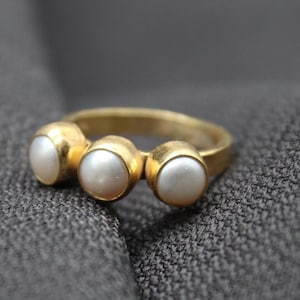 May include: A gold ring with three round white pearls set in the band.