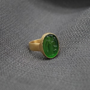 May include: A gold ring with a green oval-shaped stone featuring a carved design.