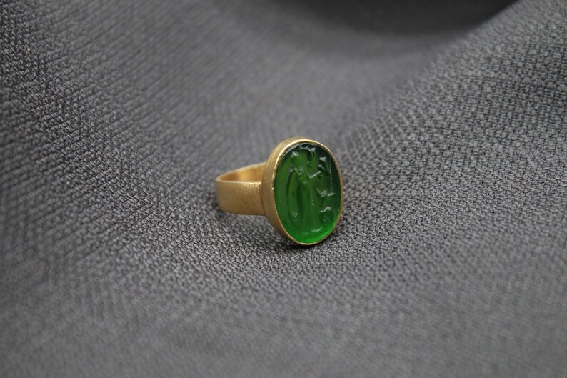 May include: A gold ring with a green oval-shaped stone featuring a carved design.
