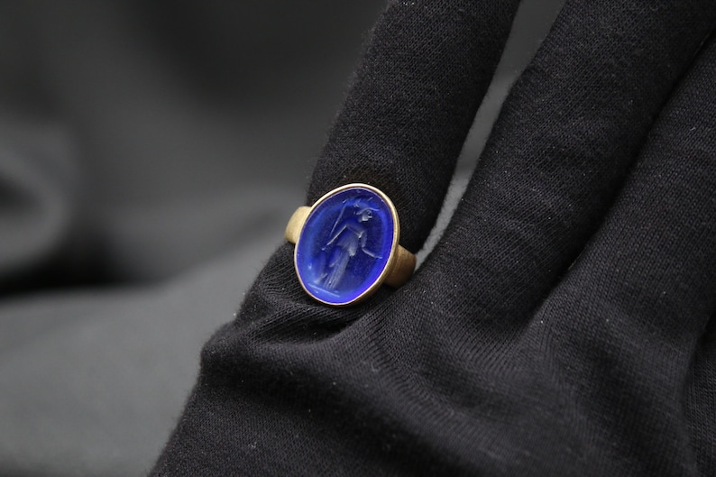 May include: A gold ring with a blue oval-shaped stone featuring an engraved image of a person.