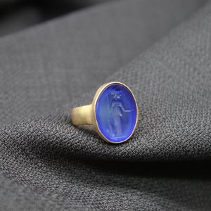 May include: A gold ring with a blue oval cameo featuring a carved image of a woman.