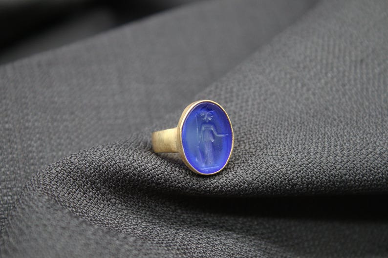 May include: A gold ring with a blue oval cameo featuring a carved image of a woman.