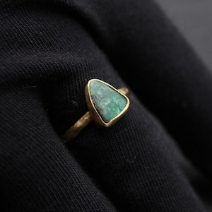 Op de afbeelding: Een gouden ring met een driehoekige groene edelsteen in het midden.