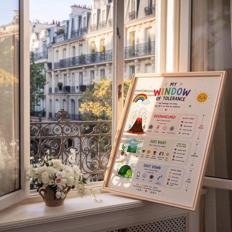 May include: A framed poster titled "My Window of Tolerance" with colorful illustrations of a rainbow, volcano, and sun. The poster is propped up on a windowsill with a view of a European city and a vase of white flowers.