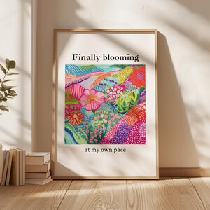 Peut inclure: Une affiche encadrée représentant un paysage floral vibrant avec le texte "Finally blooming at my own pace". L'œuvre d'art présente un éventail coloré de fleurs dans des tons de rose, rouge, bleu et vert, sur fond blanc.