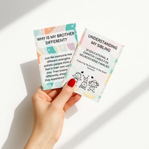 May include: Two educational cards are held in a hand. The card on the left says "WHY IS MY BROTHER DIFFERENT?" and the card on the right says "UNDERSTANDING MY SIBLING". The cards have colorful pastel designs and text.