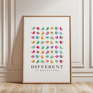 Op de afbeelding: Een ingelijste kunstdruk met een raster van kleine, kleurrijke cartoonvogels in tinten roze, geel, taling en paars. Onder de vogels staat de tekst "DIFFERENT IS BEAUTIFUL" in een vetgedrukt, zwart, schreefloos lettertype op een witte achtergrond.