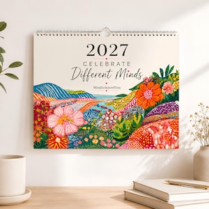 Op de afbeelding: Een wandkalender voor 2027 met de titel Celebrate Different Minds van MindScience4You. De omslag toont een levendige, kleurrijke landschapsillustratie met gestileerde bloemen, glooiende heuvels en een kustgezicht in oranje, roze en groene tinten.