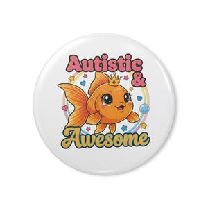 Può includere: Un bottone bianco con un pesce rosso dei cartoni animati con una corona. Il testo "Autistic & Awesome" è visualizzato in un carattere colorato e giocoso, circondato da stelle, cuori e un arcobaleno.