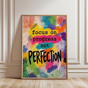 Könnte beinhalten: Ein rechteckiger Wandkunstdruck in einem hellen Holzrahmen mit einem bunten abstrakten Hintergrund aus Gekritzel, Punkten und Wirbeln in Gelb, Pink, Blau, Grün und Orange. Der Text lautet focus on progress not PERFECTION in Schwarz.