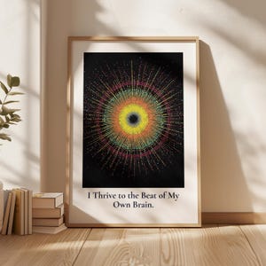 Può includere: Una stampa artistica incorniciata che presenta un'esplosione circolare centrale di punti colorati in giallo, arancione, rosso e turchese su sfondo nero. Sotto la grafica, il testo recita: I Thrive to the Beat of My Own Brain. La cornice è in legno chiaro.